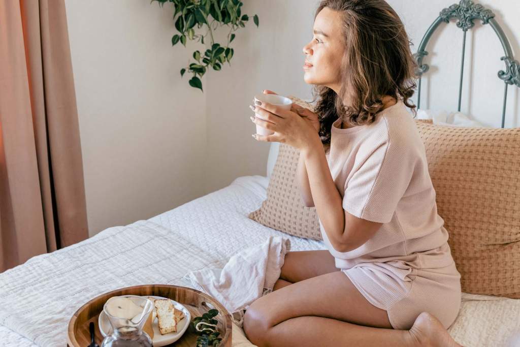  A young woman in cozy pajamas, sitting on a bed surrounded by soft pillows and fairy lights, holding a cup of herbal tea and reading a book, creating a peaceful and relaxing atmosphere for her nighttime routine.