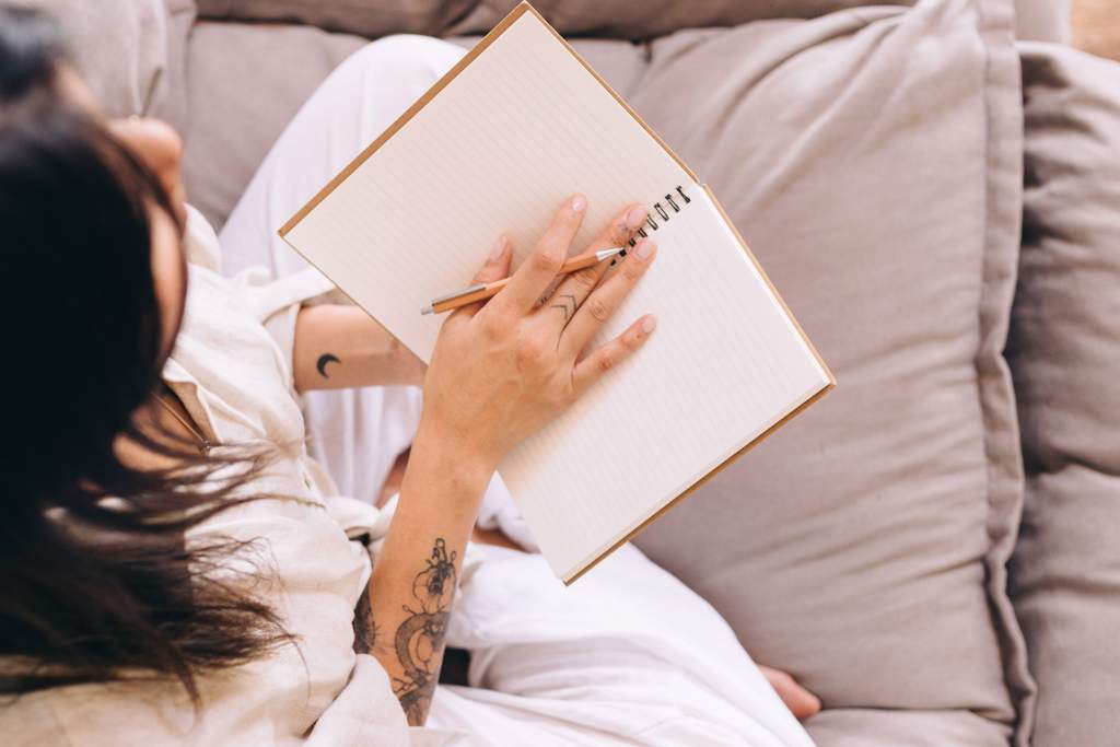 Image of a woman relaxing on her bed while writing down her gratitude list - This is about how to make your A to Z gratitude list