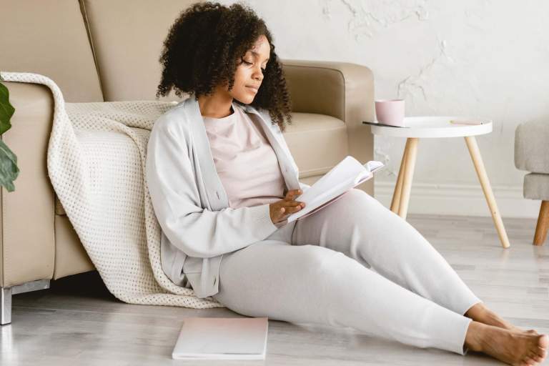 A woman sitting with a notebook with 'November Goals' written on a crisp page, accompanied by a cup of warm coffee, evoking a sense of motivation and planning for the month ahead. She is planing her goals for November.