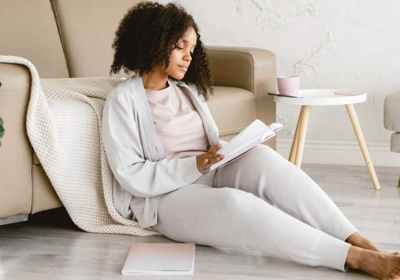 A woman sitting with a notebook with 'November Goals' written on a crisp page, accompanied by a cup of warm coffee, evoking a sense of motivation and planning for the month ahead. She is planing her goals for November.