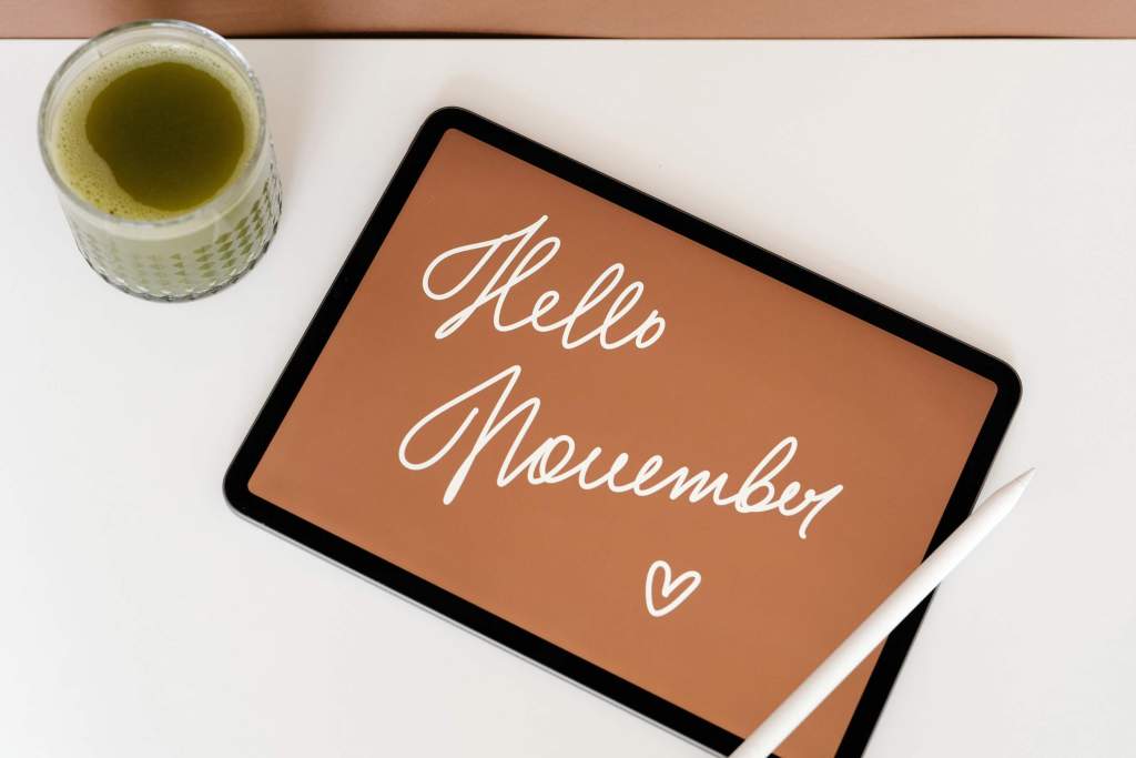 "Image: An iPad with 'November Goals' written on it accompanied by a cup of warm green juice. The scene is set against a backdrop of autumn color, evoking a sense of motivation and planning for the month ahead."
