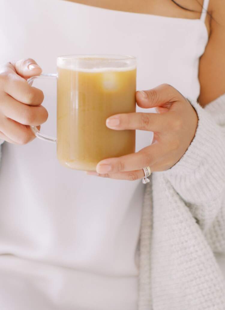 A woman in a cozy sweater holds a cup of coffee, enjoying her quick morning routine with a refreshing drink of water.