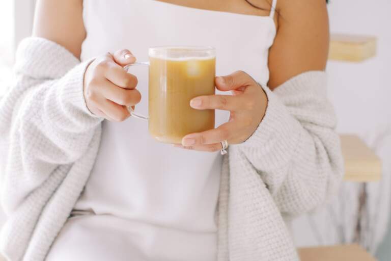 A woman in a cozy sweater holds a cup of coffee, enjoying her quick morning routine with a refreshing drink of water.