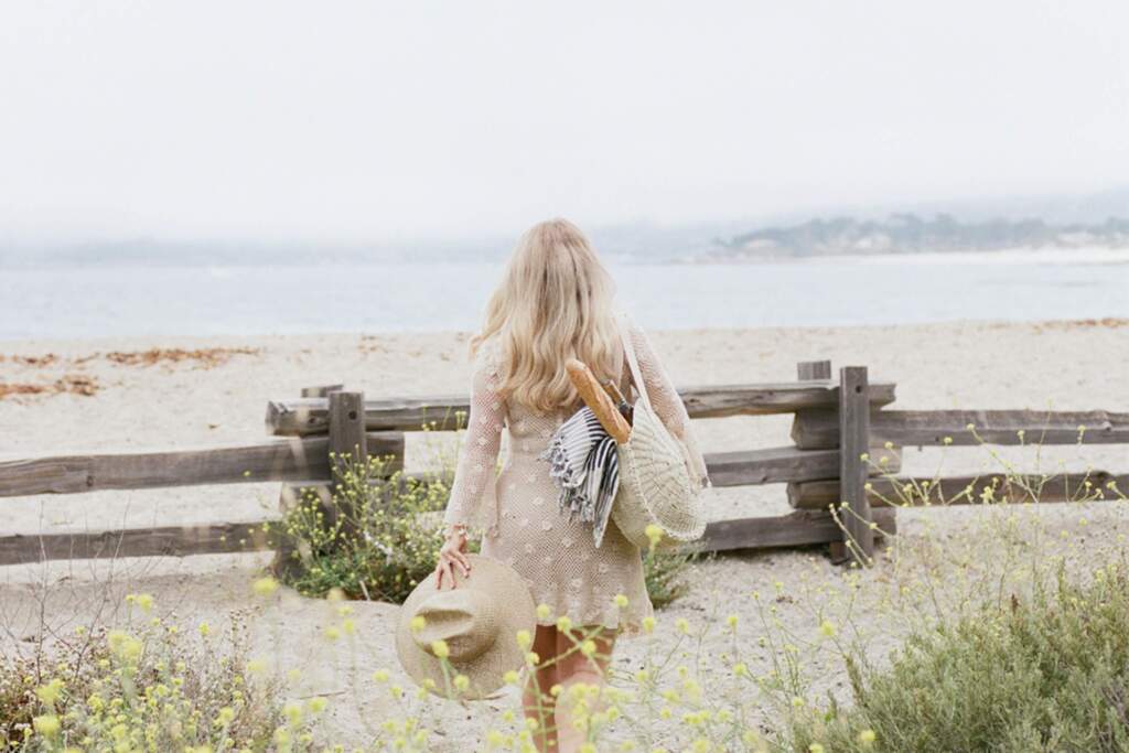This captivating image showcases a woman, wearing a hat and carrying a bag, walking along the beach, perfectly embodying the essence of summer affirmations.