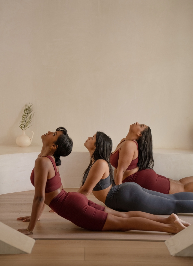 Image of three women in yoga attire performing a downward dog pose. Featured in a blog post on feminine energy traits