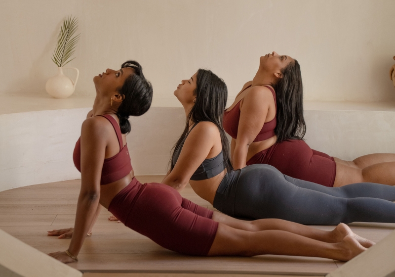 Image of three women in yoga attire performing a A downward dog pose. Featured in a blog post on feminine energy traits