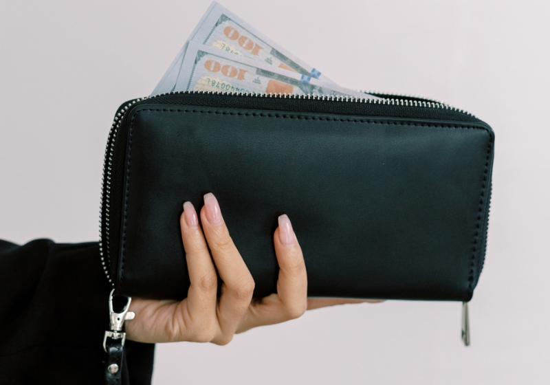 A woman holding a black wallet with money inside. Featured image in a money manifestation blog post.