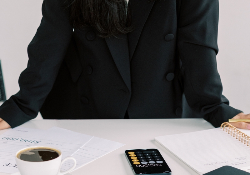 Featured image for a money affirmations blog post: woman in business suit at desk with laptop and coffee.