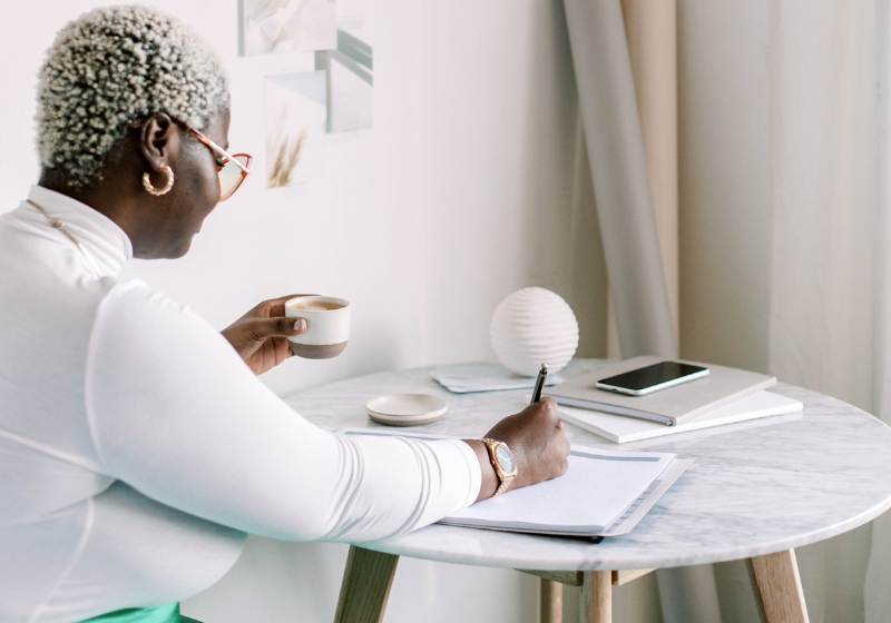 A lady writing morning pages with a cup of coffee at a table