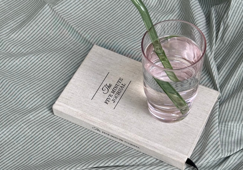 Feminine energy traits showcased with a book, water glass, and plant on a bed.