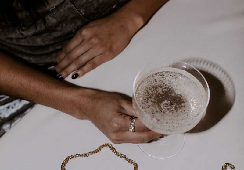 A stylish woman holds a gold clutch and a glass of champagne, embodying elegance and high vibrational energy