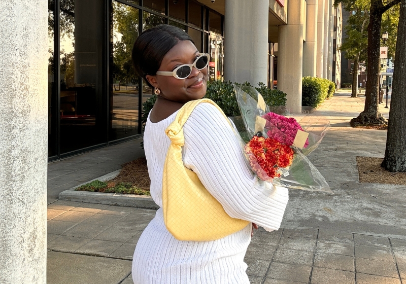 A woman in a cozy white sweater holds a bright yellow purse, radiating positive energy, featured image in a blog post about signs of high vibration person