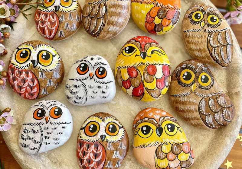 Hand-painted owl illustrations on rocks, displayed on a wooden surface. These are called Kindness rocks and it's an aesthetic thing to do by yourself