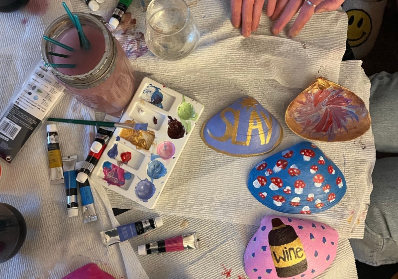 Crafting table with painted rocks, acrylic paints, palette, and a paintbrush.