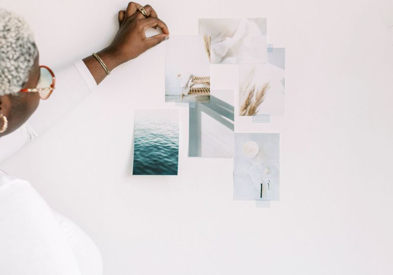 Person arranging aesthetic photos of nature and textures on a white wall, exploring images for vision board, as one of the most soothing aesthetic things to do when bored.