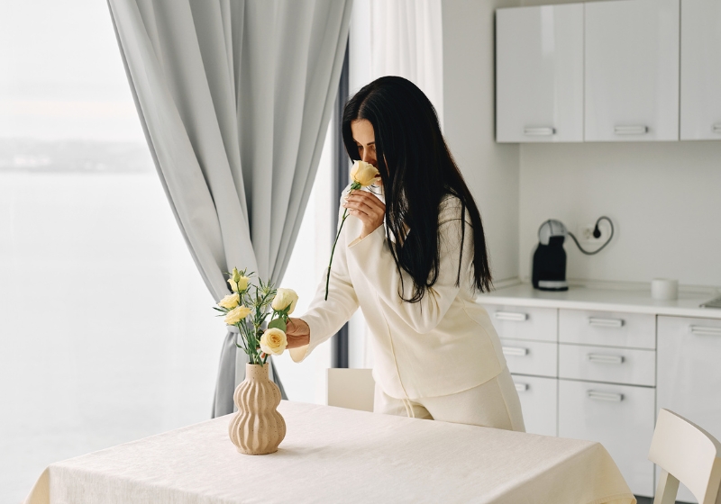 A woman arranging pale yellow roses in a vase, pausing to smell a flower, evoking serenity and mindfulness—ideal for setting an intentional space for protective affirmations