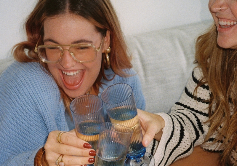 Two friends laughing and clinking glasses in a moment of celebration, radiating joy and connection. Their warm smiles and casual setting capture the essence of supportive friendship