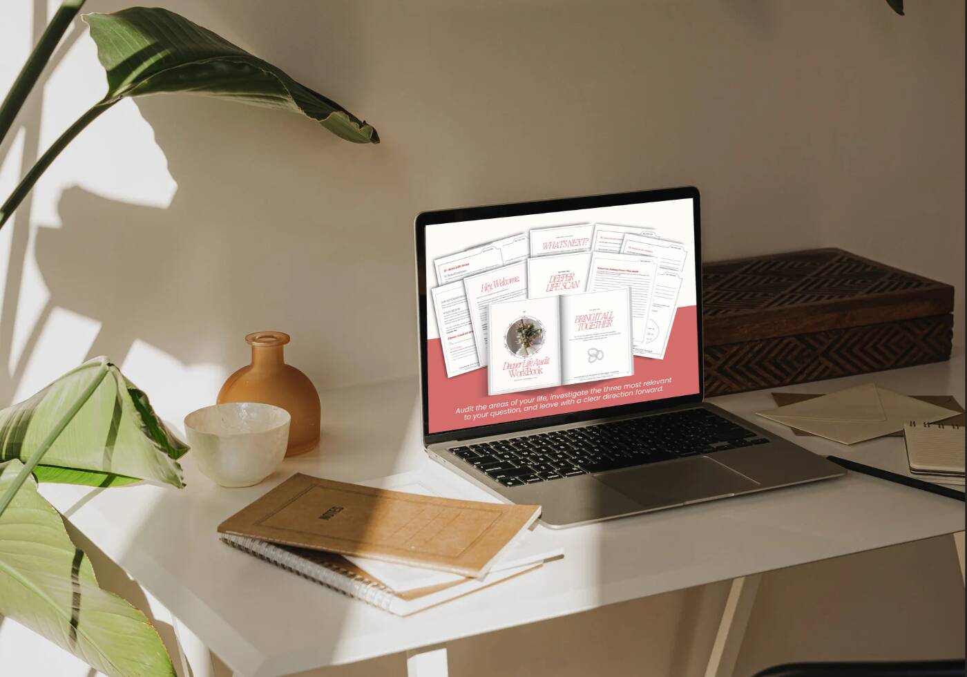 Laptop displaying the Deeper Life Audit Workbook with guided worksheets for assessing different areas of life, set on a sunlit desk with notebooks, a ceramic cup, and green plants.